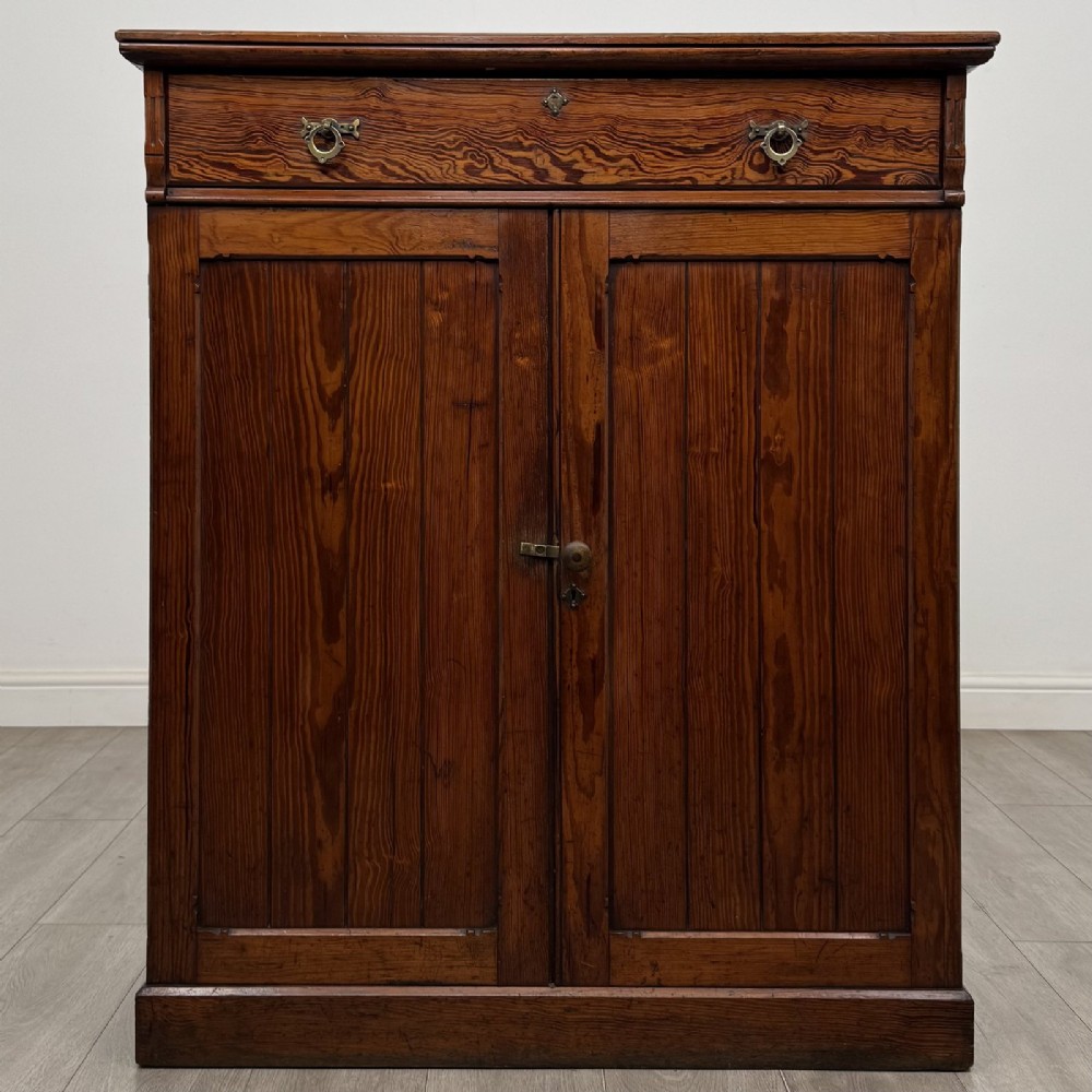 A Victorian pitch pine cupboard featuring a single top drawer with brass drop ring handles above a two-door cabinet with vertical panelled detailing.
