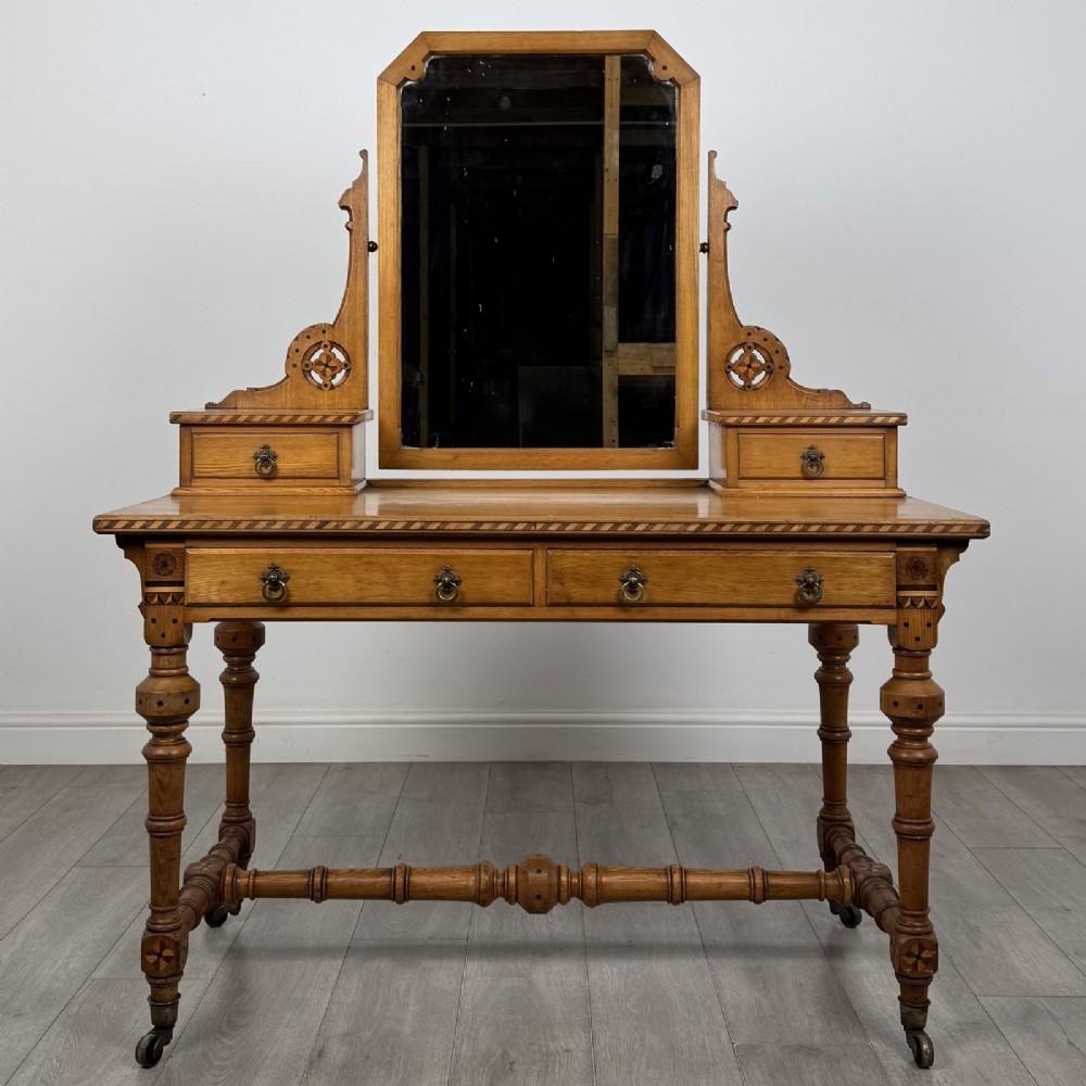 An antique Victorian Gothic oak dressing table featuring a central adjustable swing mirror, pierced tracery supports, two upper trinket drawers, two main drawers, inlaid borders, turned legs, and brass ring handles.