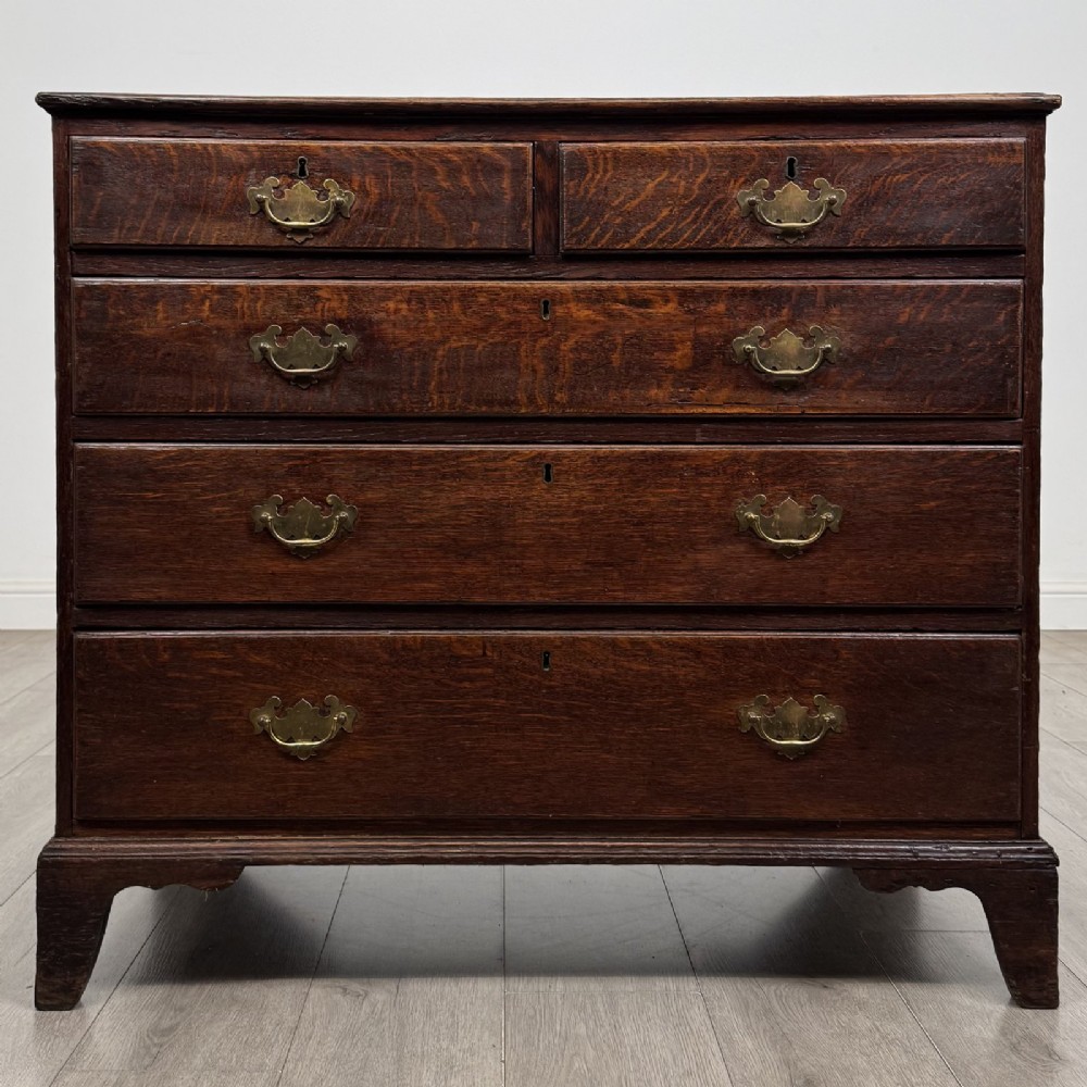 An 18th-century dark oak Georgian chest of drawers featuring a two-short-over-three-long drawer configuration, brass handles, and bracket feet.