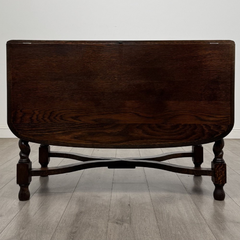 A dark brown oak drop-leaf dining table with folded side leaves, barley twist legs, and a shaped cross-stretcher base.