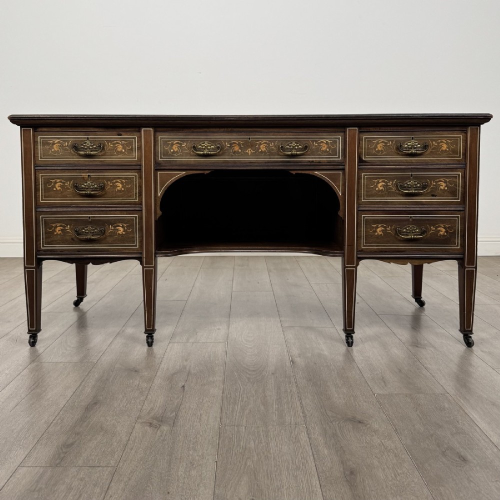 An Edwardian mahogany sideboard featuring detailed foliate marquetry inlay, seven drawers with brass handles, an arched central apron, and tapered legs with castors.