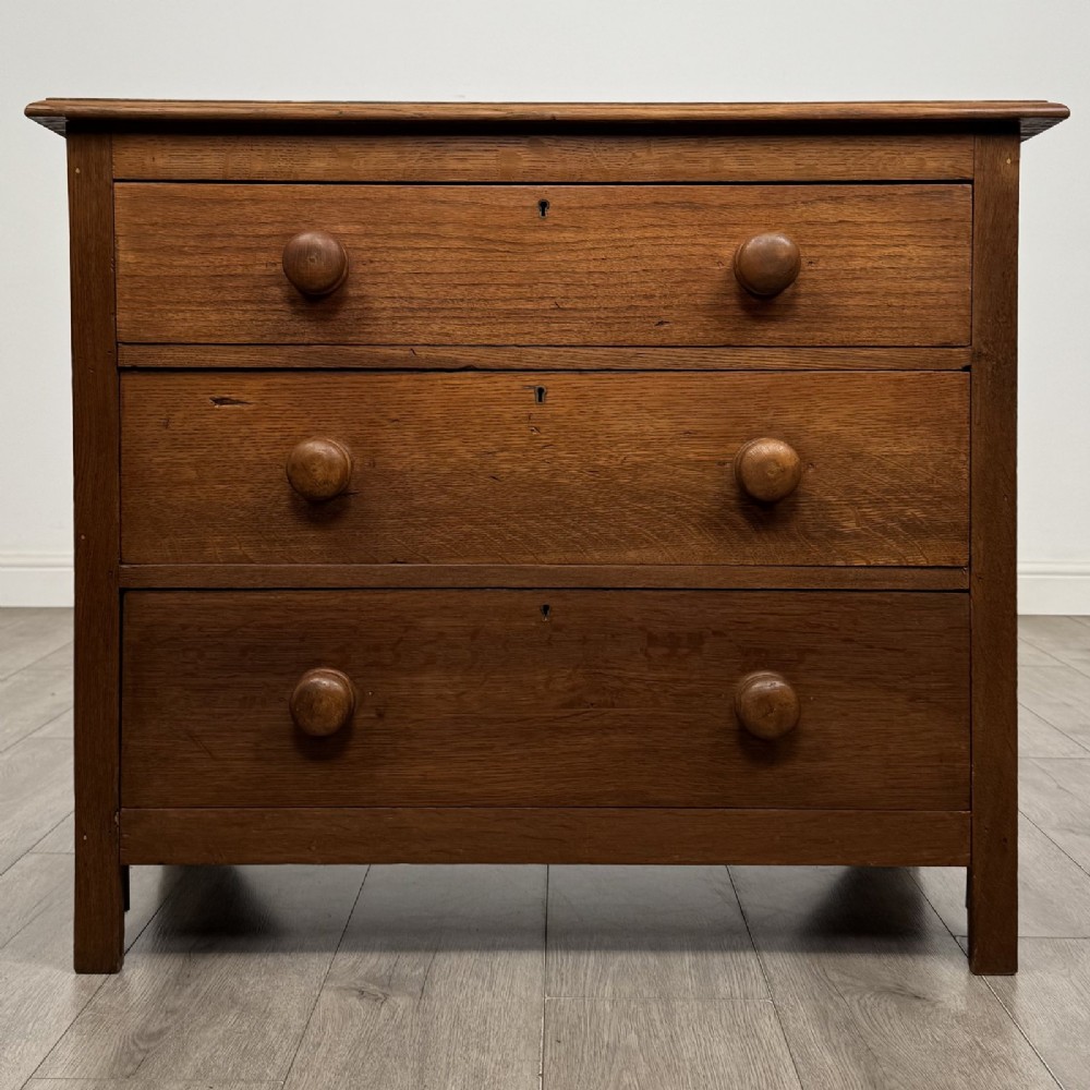 A small 20th-century warm brown oak chest of drawers featuring three wide drawers with turned wooden knobs.