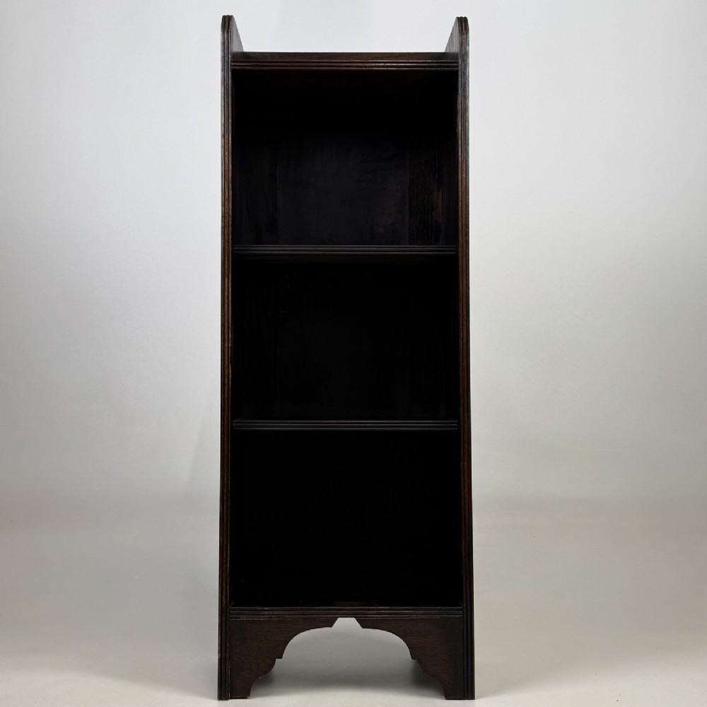 A tall narrow dark oak open bookcase featuring a gallery top and three shelves above a shaped base.