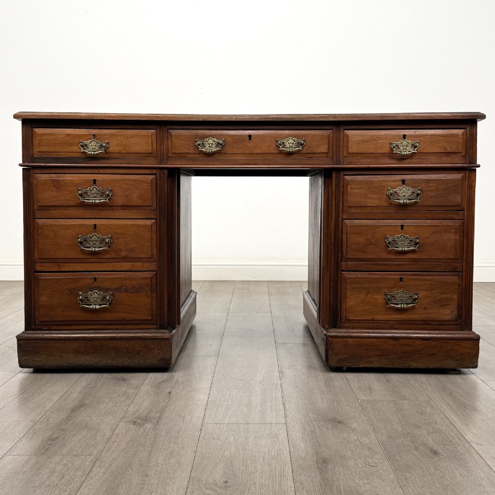 A 19th-century walnut pedestal desk featuring nine drawers with brass handles and a plinth base.