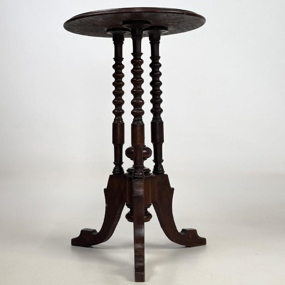 A dark brown Victorian lamp table featuring a circular circular top supported by three bobbin-turned upright columns on a tripod base.