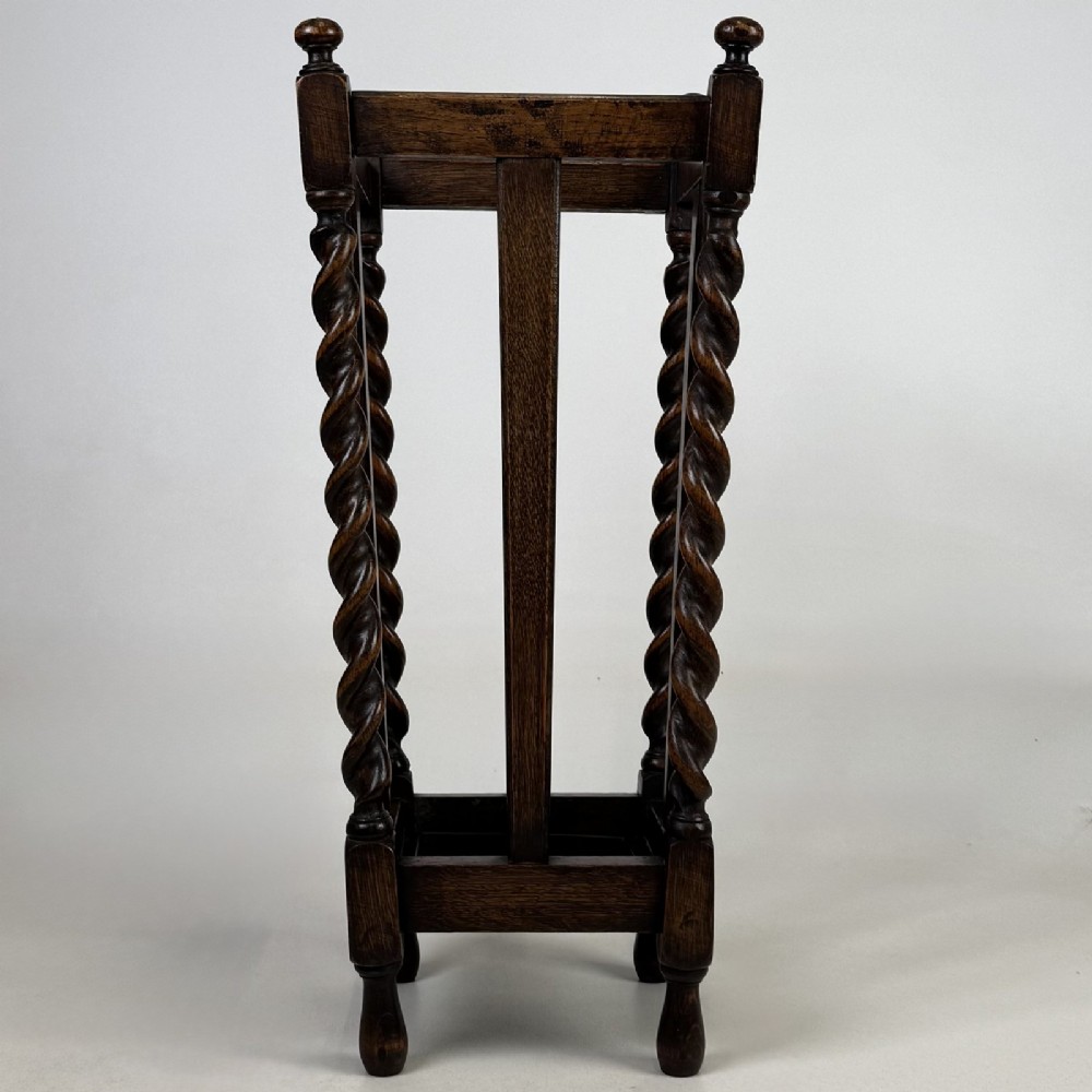 An early 20th-century dark oak umbrella stand featuring four barley twist columns topped with small finials.