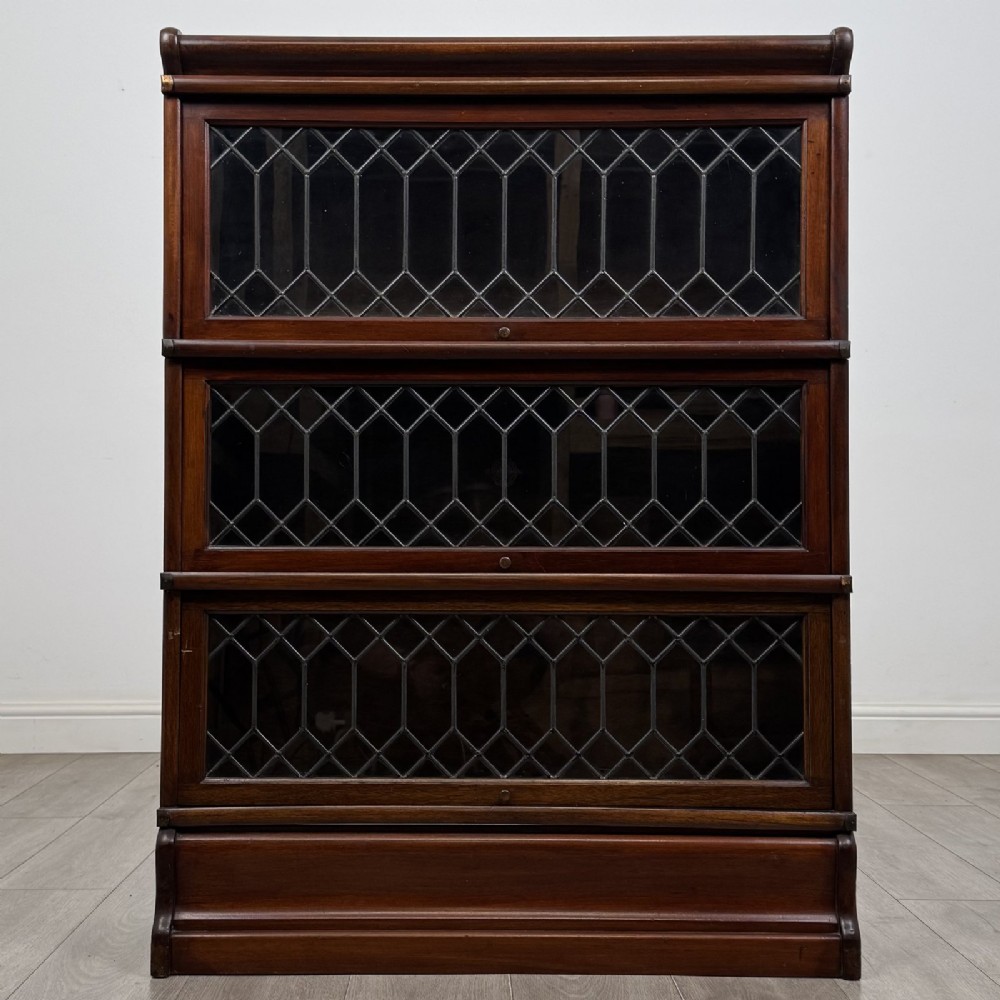 A three-tier dark mahogany Globe Wernicke sectional bookcase featuring geometric leaded glass doors.