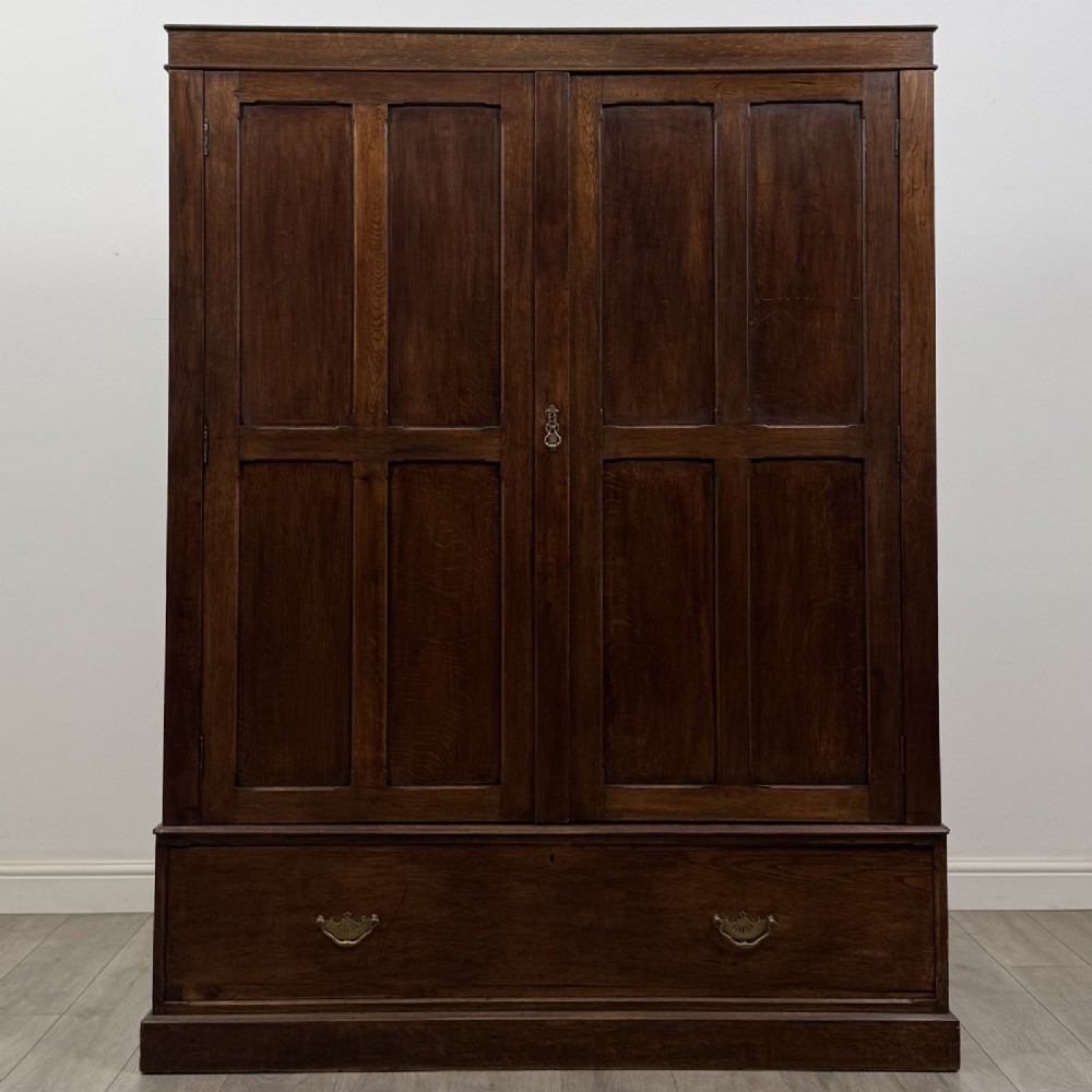 A tall dark oak Edwardian wardrobe featuring double panelled doors above a single full-width base drawer with brass drop handles.