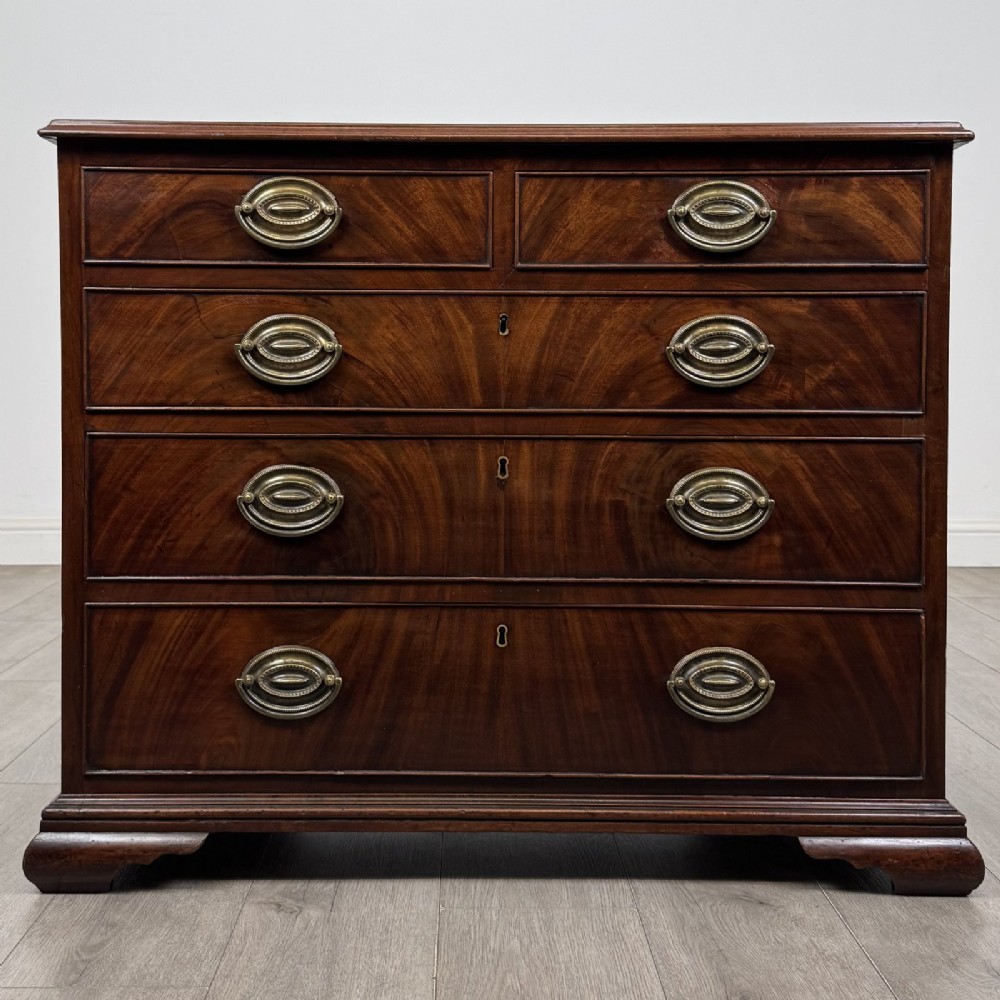 An 18th-century Georgian dark mahogany chest of drawers featuring a two-over-three drawer arrangement with oval brass handles and bracket feet.