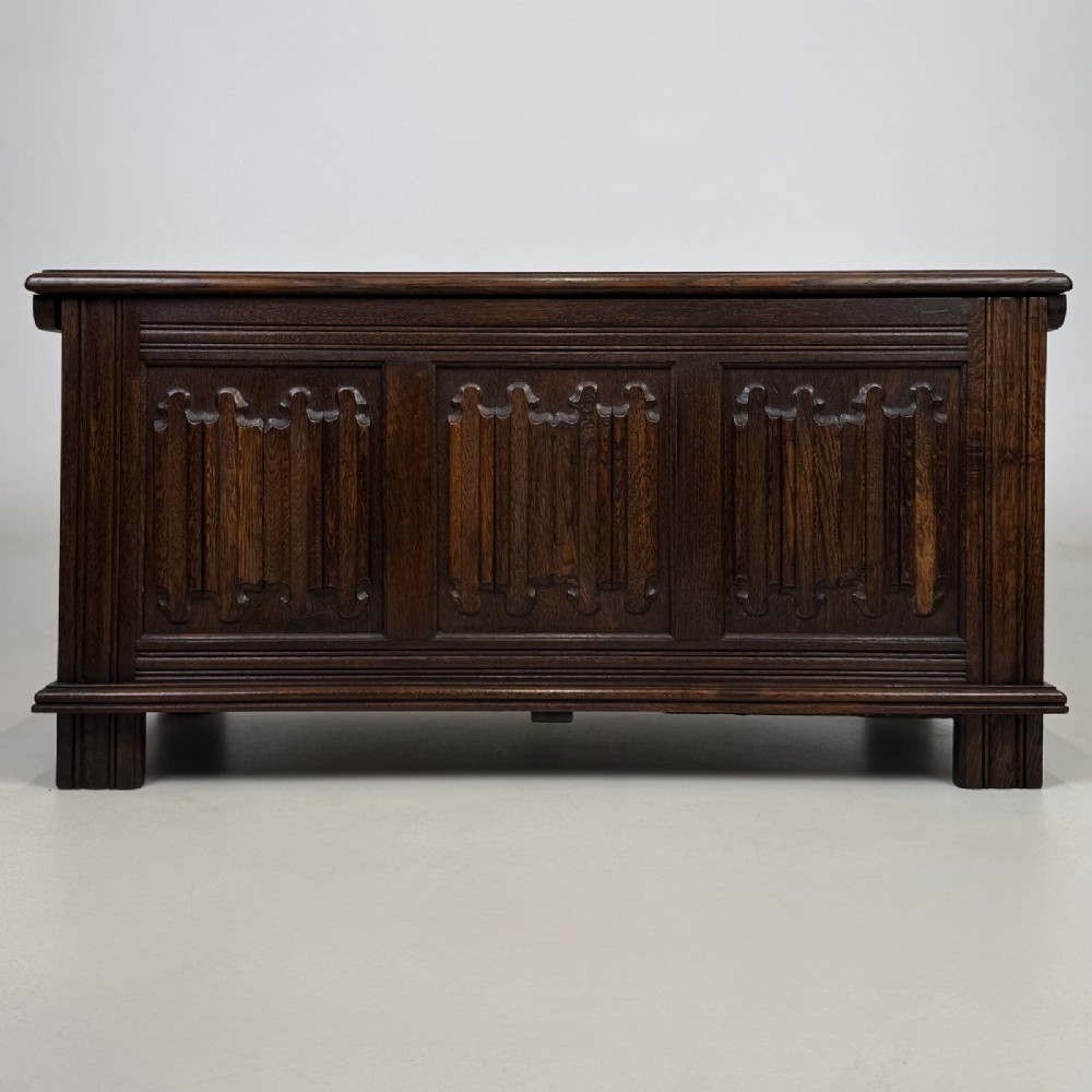 A rectangular dark oak coffer with three carved linenfold panels along the front facade.