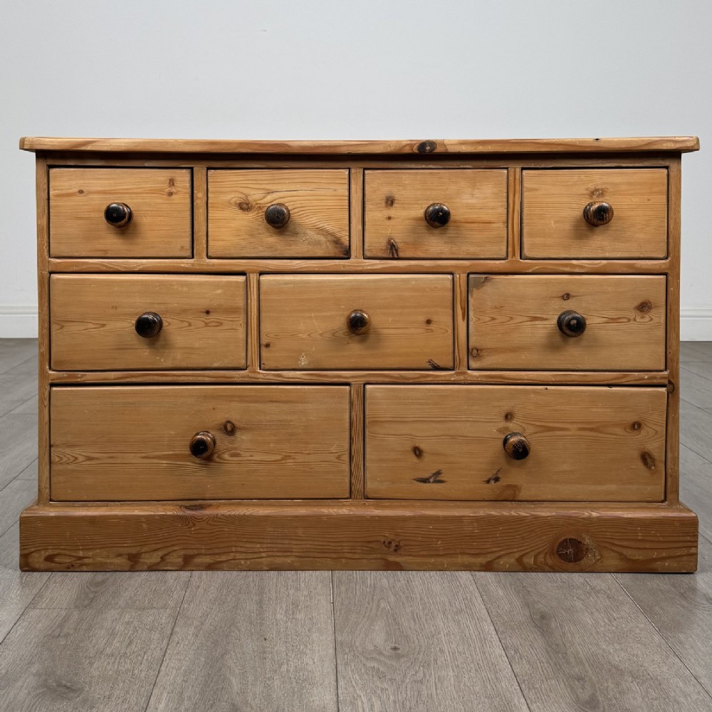 A 20th-century pine chest of drawers featuring nine multi-sized drawers with dark turned wooden knobs arranged on a solid plinth base.