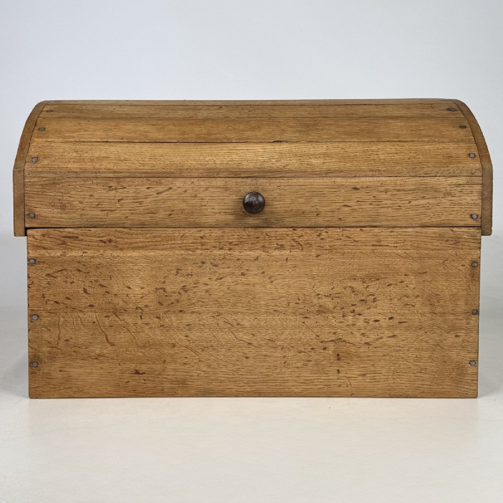 A small light oak storage chest featuring a curved domed lid, metal stud details along the side edges, and a central wooden knob on the front.
