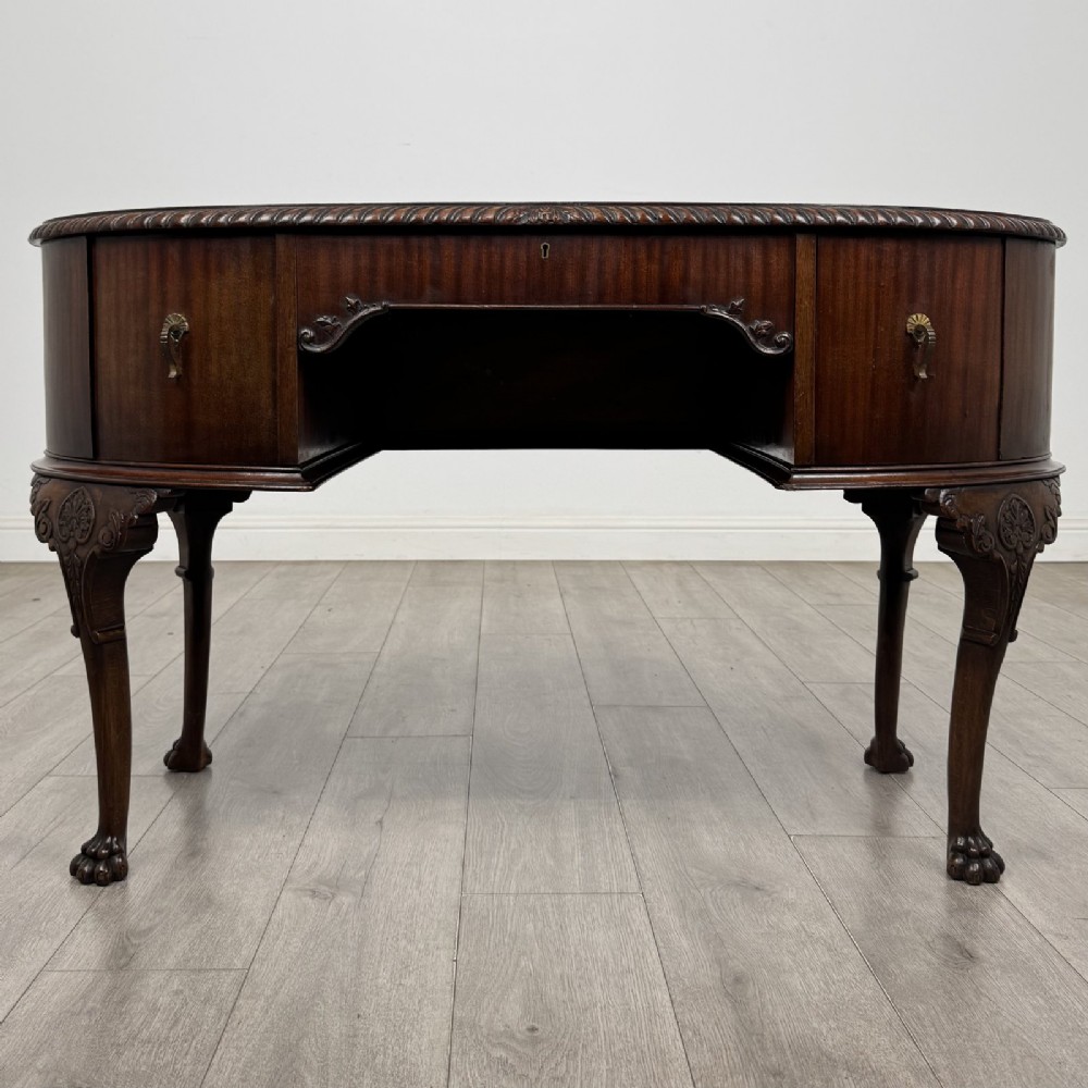 A Chippendale style mahogany oval desk featuring cabriole legs with carved knees, ball-and-claw feet, side drawers, and a central kneehole.