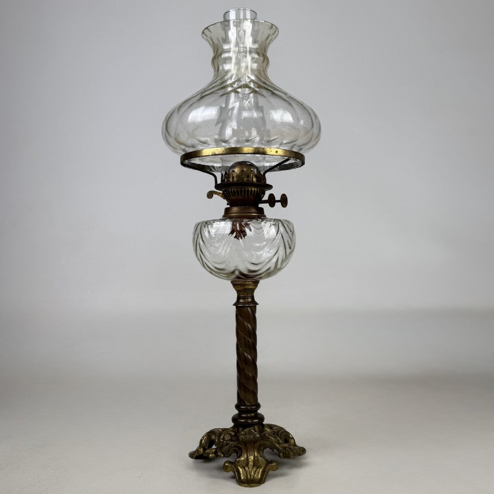 A 19th-century brass oil lamp featuring a cast footed base, a spiral twisted column, a clear swirled glass reservoir, and a matching swirled glass shade.