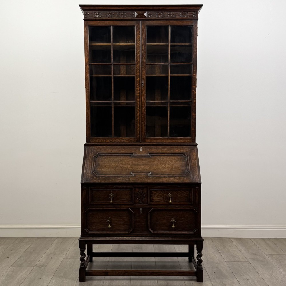 A dark oak bureau bookcase with upper glazed doors, a fall-front desk flap, lower drawers, and turned barley twist legs.