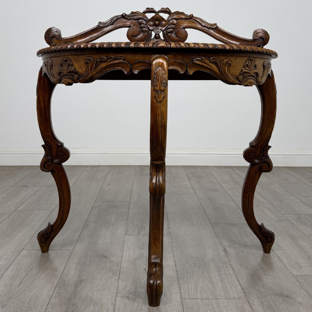 A semicircular carved wooden demi-lune console table featuring cabriole legs, an ornate raised gallery back with carved floral motif, and a gadrooned top edge.