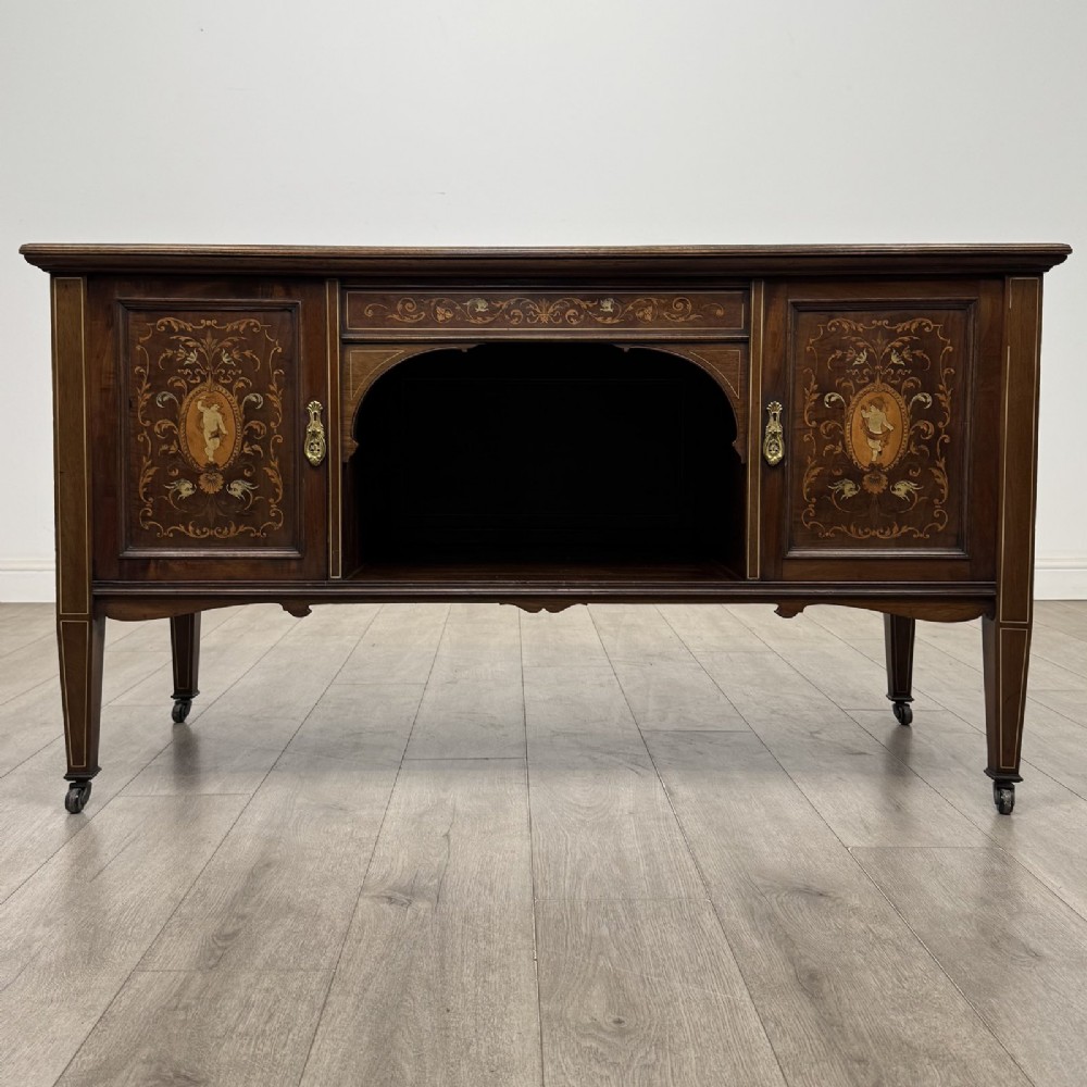 An Edwardian inlaid mahogany sideboard with cherub marquetry panels, a central arched alcove, drawer, and square tapered legs with castors.