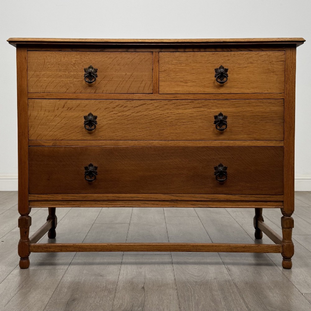 An antique oak chest of drawers featuring two short drawers above two long drawers, metal drop handles, turned legs, and a lower stretcher rail.