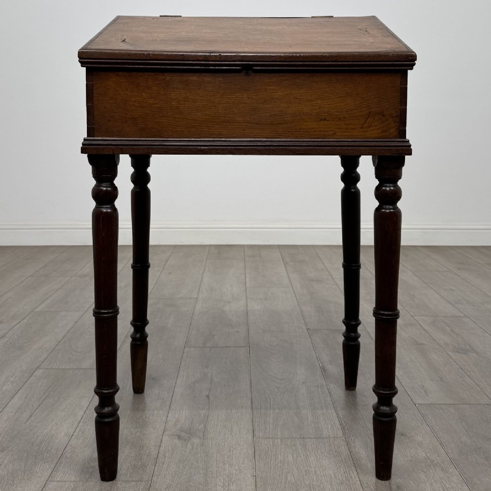 A small dark oak Victorian clerks desk with a sloped hinged lid raised on tall turned legs.
