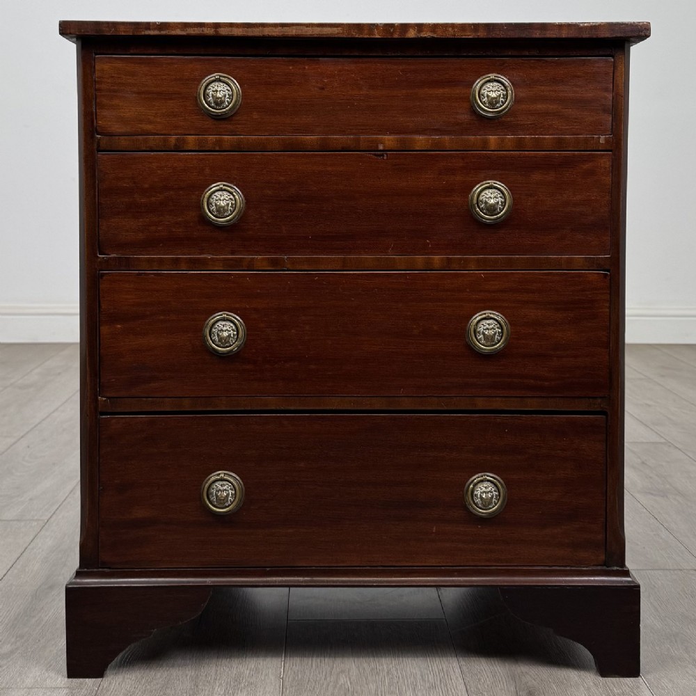 A small Georgian-style dark mahogany chest of four drawers featuring brass ring pull handles and bracket feet.