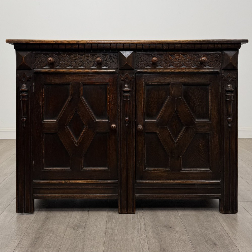 A dark oak Jacobean style sideboard featuring two upper carved drawers and two cupboard doors decorated with geometric diamond panels.