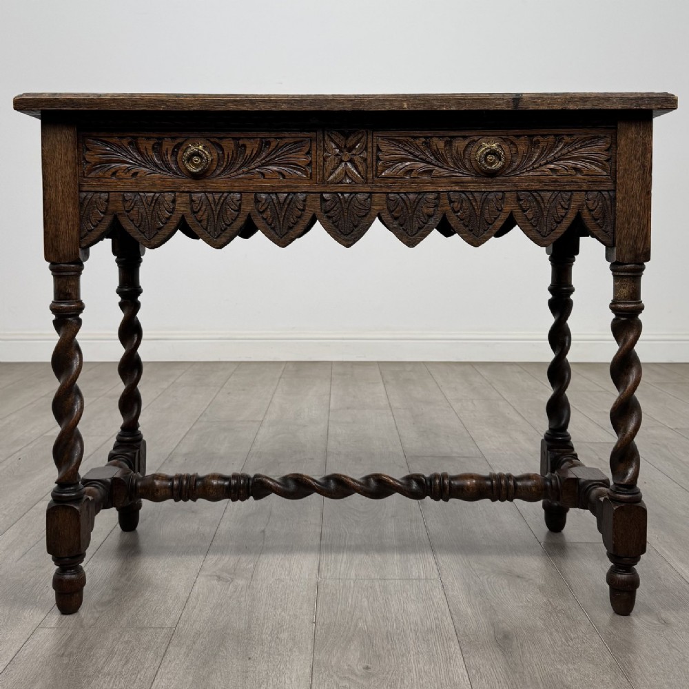 A dark oak Victorian side table featuring hand-carved foliate drawers, a scalloped lower apron, and four barley twist legs joined by a central stretcher.
