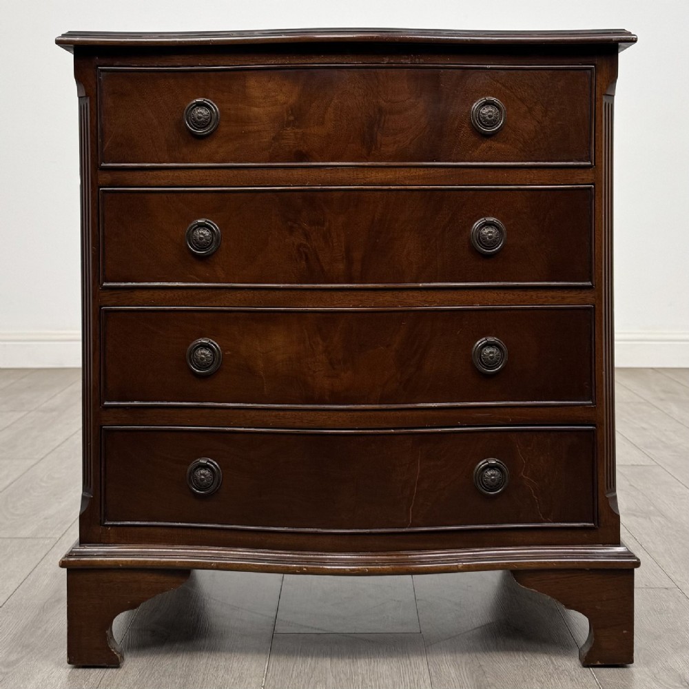 A dark brown mahogany Georgian style chest of drawers featuring four drawers, fluted side pilasters, circular handles, and bracket feet.