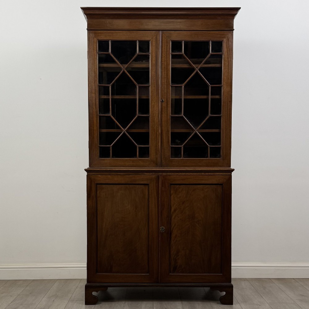 An antique Georgian mahogany two-section bookcase featuring upper double doors with geometric astragal glazing over lower solid panelled cupboard doors, supported by bracket feet.