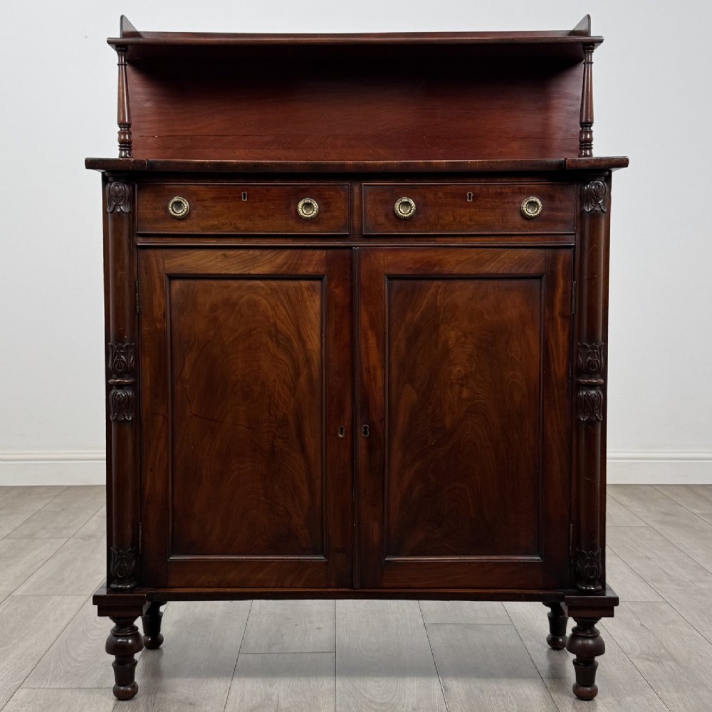 A Regency mahogany chiffonier featuring a raised shelf, two drawers with brass ring handles, and a double-door cupboard flanked by carved columns on turned feet.