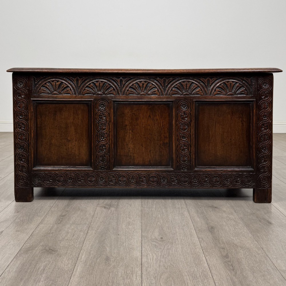 A dark oak Jacobean style blanket box featuring a carved lunette frieze, three panelled sections, and guilloche carving along the stiles.