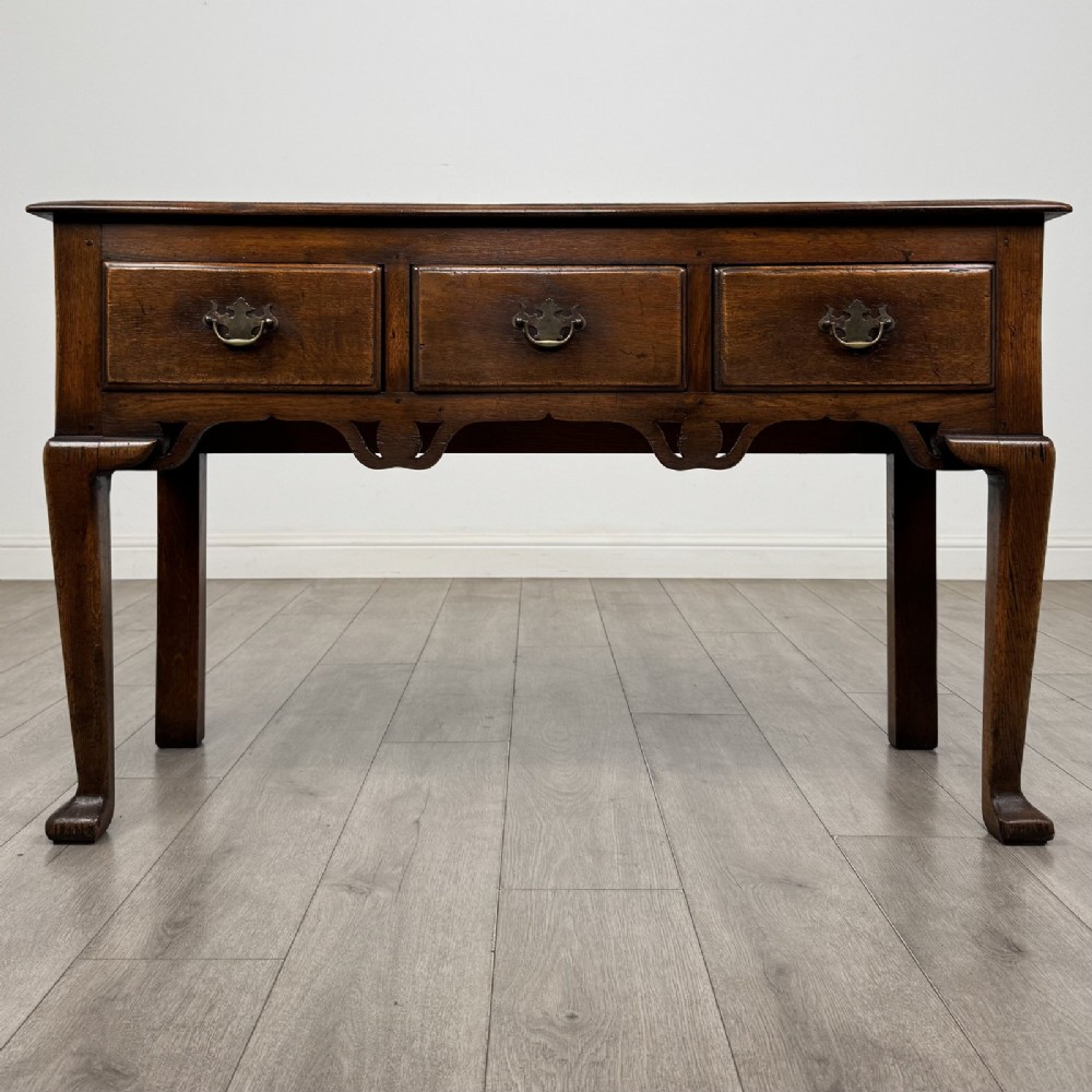 A Georgian style dark oak dresser base featuring three drawers with brass swan-neck handles, a shaped apron, and cabriole front legs.