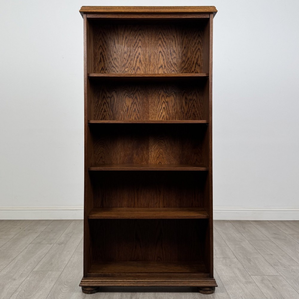 A tall dark oak open bookcase with five tiered compartments, adjustable shelves, a moulded cornice, and flattened bun feet.