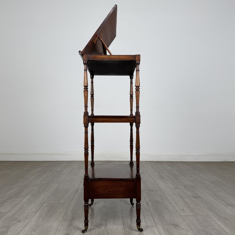 An antique Regency rosewood three-tiered whatnot featuring an adjustable angled reading slope top, slender turned upright supports, a bottom drawer, and brass castors. View IV