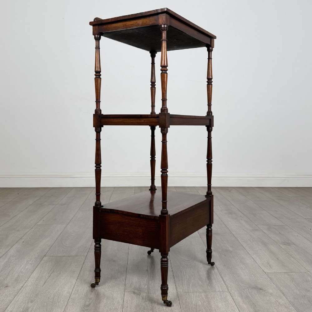 An antique Regency rosewood three-tiered whatnot featuring an adjustable angled reading slope top, slender turned upright supports, a bottom drawer, and brass castors. View VI