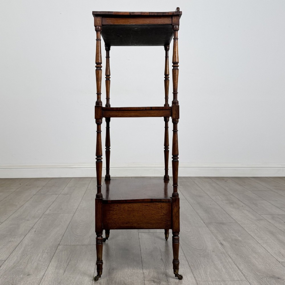 An antique Regency rosewood three-tiered whatnot featuring an adjustable angled reading slope top, slender turned upright supports, a bottom drawer, and brass castors. View IX