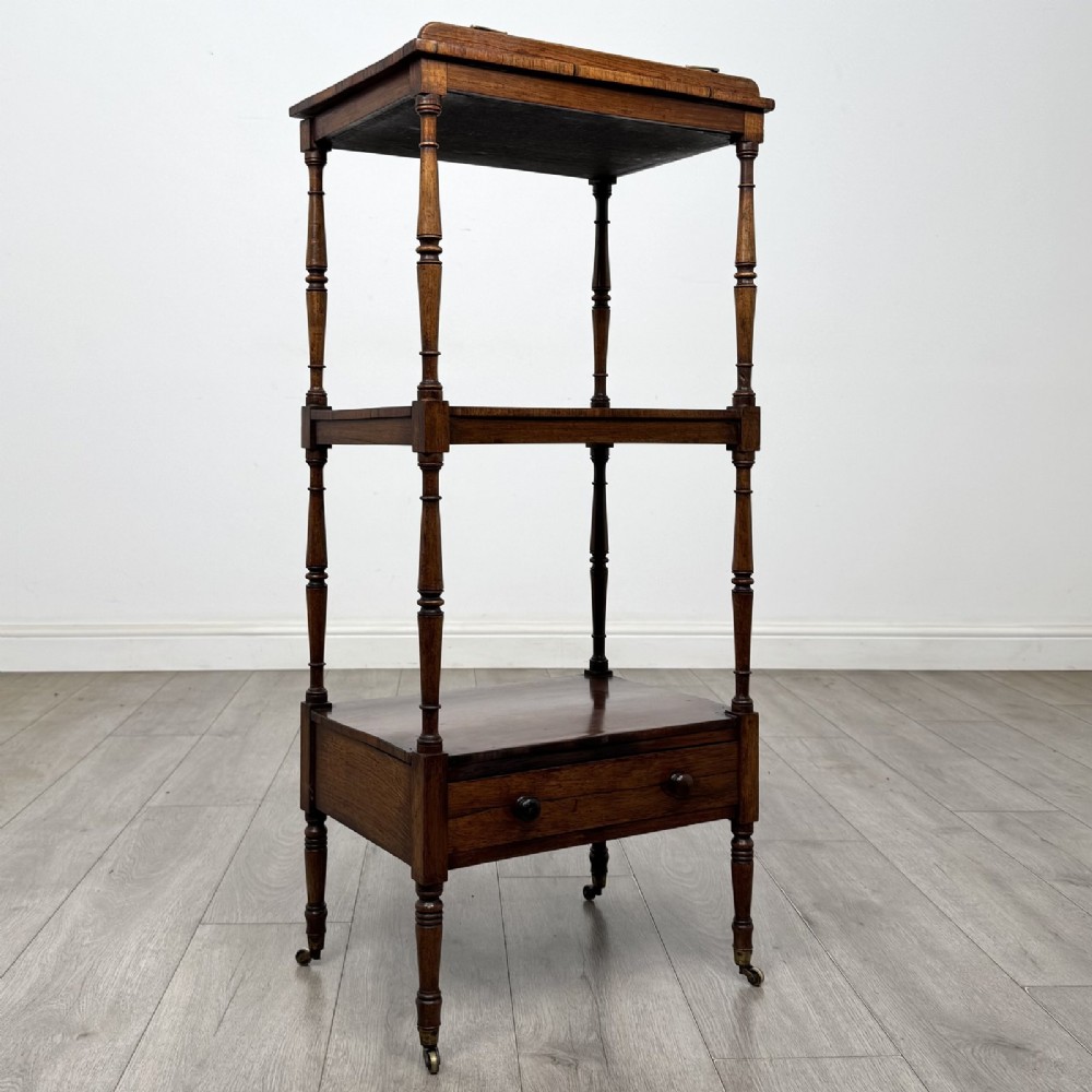 An antique Regency rosewood three-tiered whatnot featuring an adjustable angled reading slope top, slender turned upright supports, a bottom drawer, and brass castors. View X