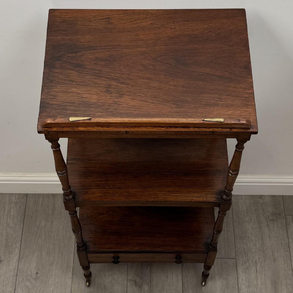 An antique Regency rosewood three-tiered whatnot featuring an adjustable angled reading slope top, slender turned upright supports, a bottom drawer, and brass castors. View XI