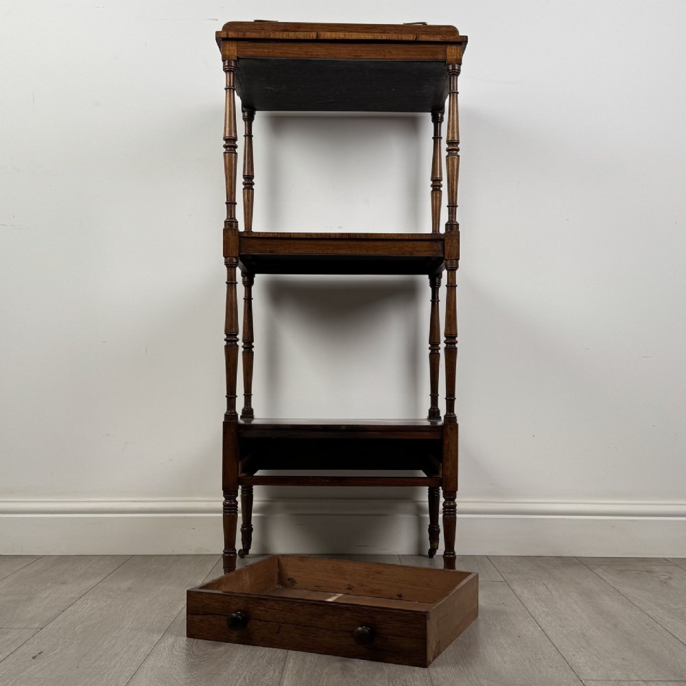 An antique Regency rosewood three-tiered whatnot featuring an adjustable angled reading slope top, slender turned upright supports, a bottom drawer, and brass castors. View XII