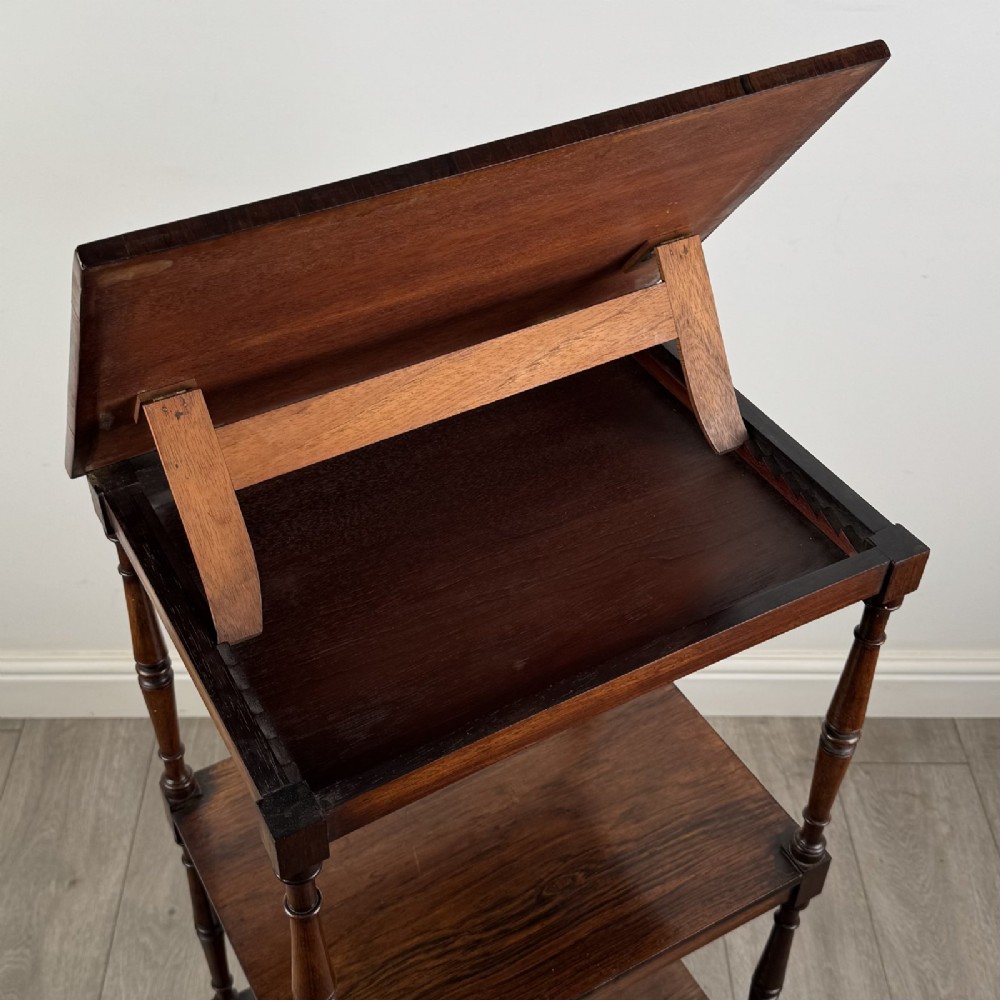An antique Regency rosewood three-tiered whatnot featuring an adjustable angled reading slope top, slender turned upright supports, a bottom drawer, and brass castors. View XIV