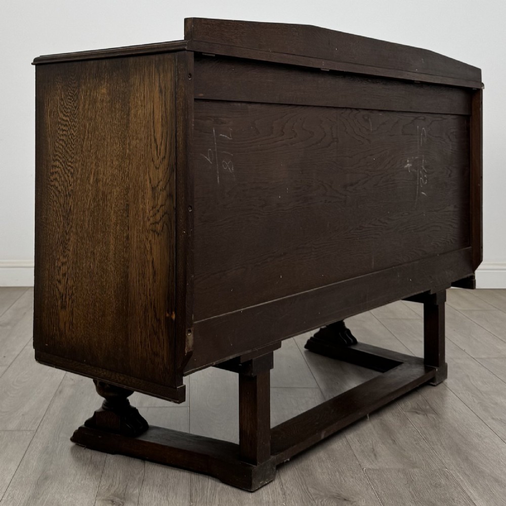 A dark brown Jacobean style oak sideboard featuring three central drawers flanked by two geometric panel cupboard doors, supported on turned legs. View V