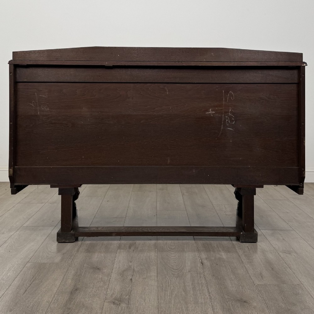 A dark brown Jacobean style oak sideboard featuring three central drawers flanked by two geometric panel cupboard doors, supported on turned legs. View VI