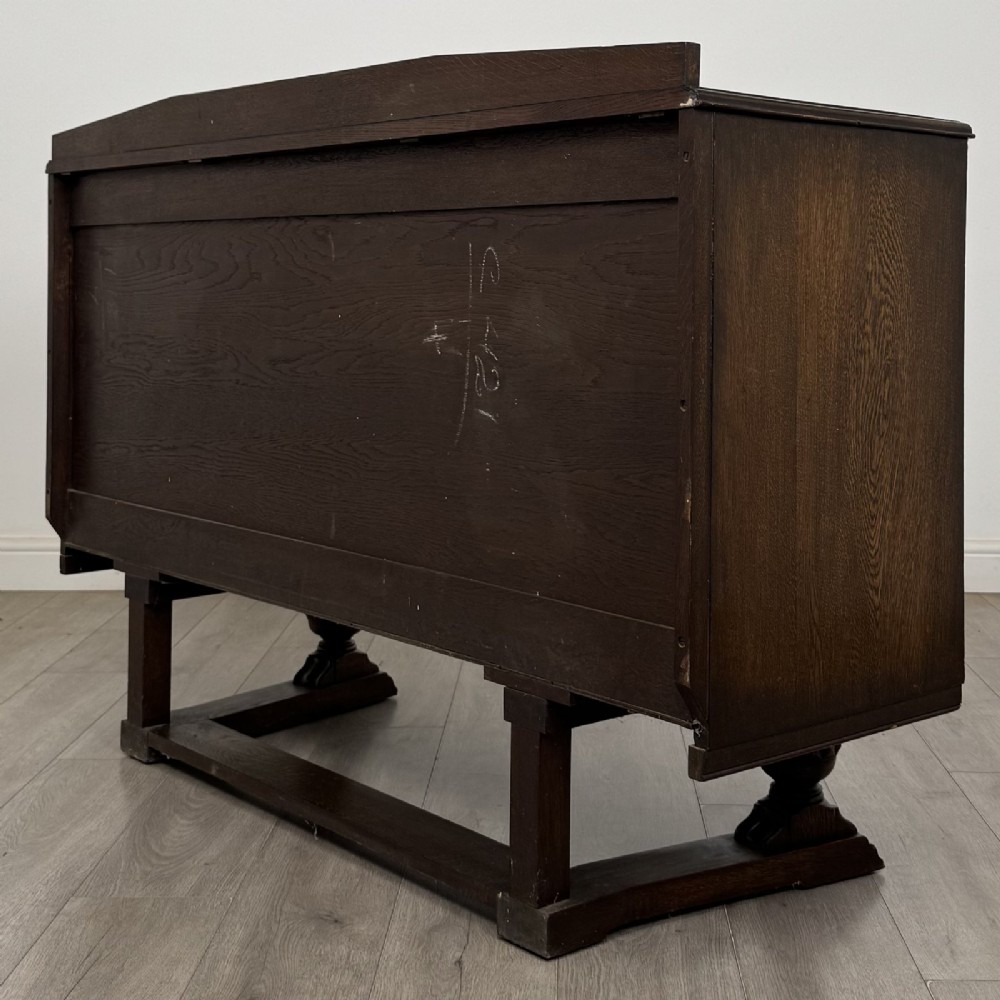 A dark brown Jacobean style oak sideboard featuring three central drawers flanked by two geometric panel cupboard doors, supported on turned legs. View VII