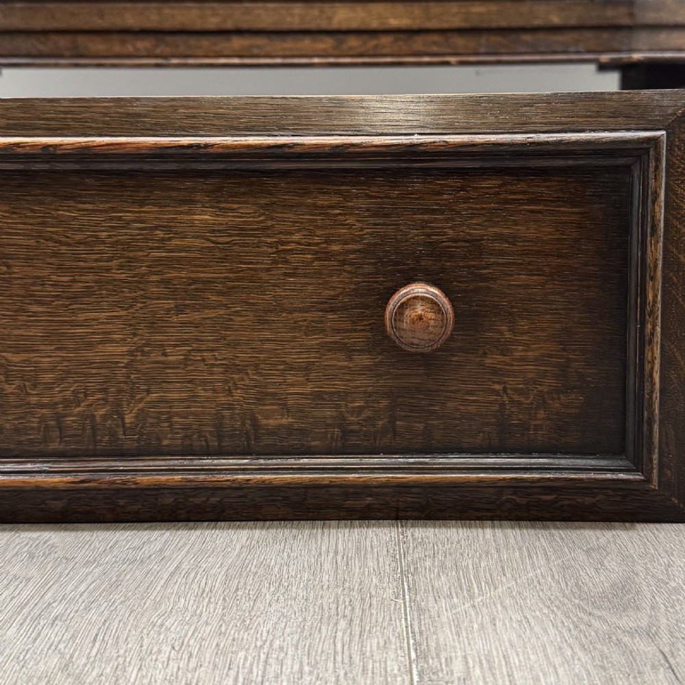 A dark brown Jacobean style oak sideboard featuring three central drawers flanked by two geometric panel cupboard doors, supported on turned legs. View XII