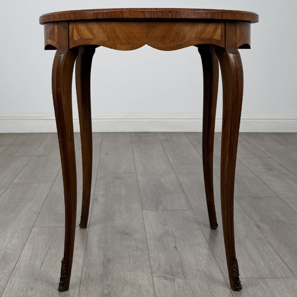 A circular French Louis XV style lamp table featuring slender cabriole legs, marquetry wood grain pattern, an undulating apron, and metal sabot feet.