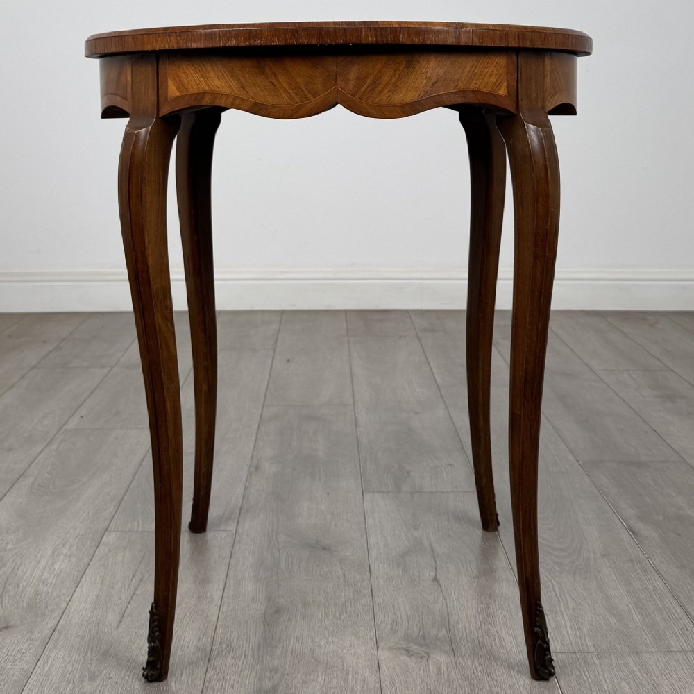 A circular French Louis XV style lamp table featuring slender cabriole legs, marquetry wood grain pattern, an undulating apron, and metal sabot feet. View III