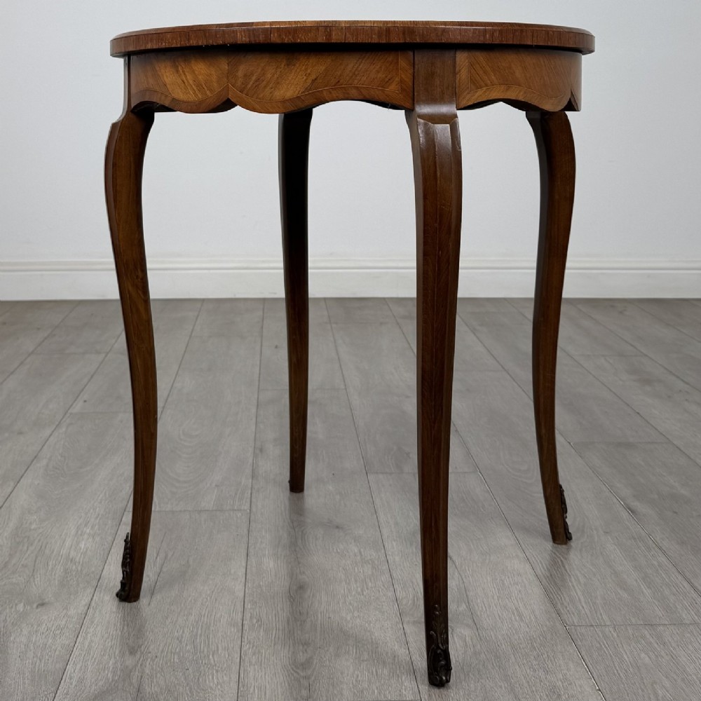 A circular French Louis XV style lamp table featuring slender cabriole legs, marquetry wood grain pattern, an undulating apron, and metal sabot feet. View IV