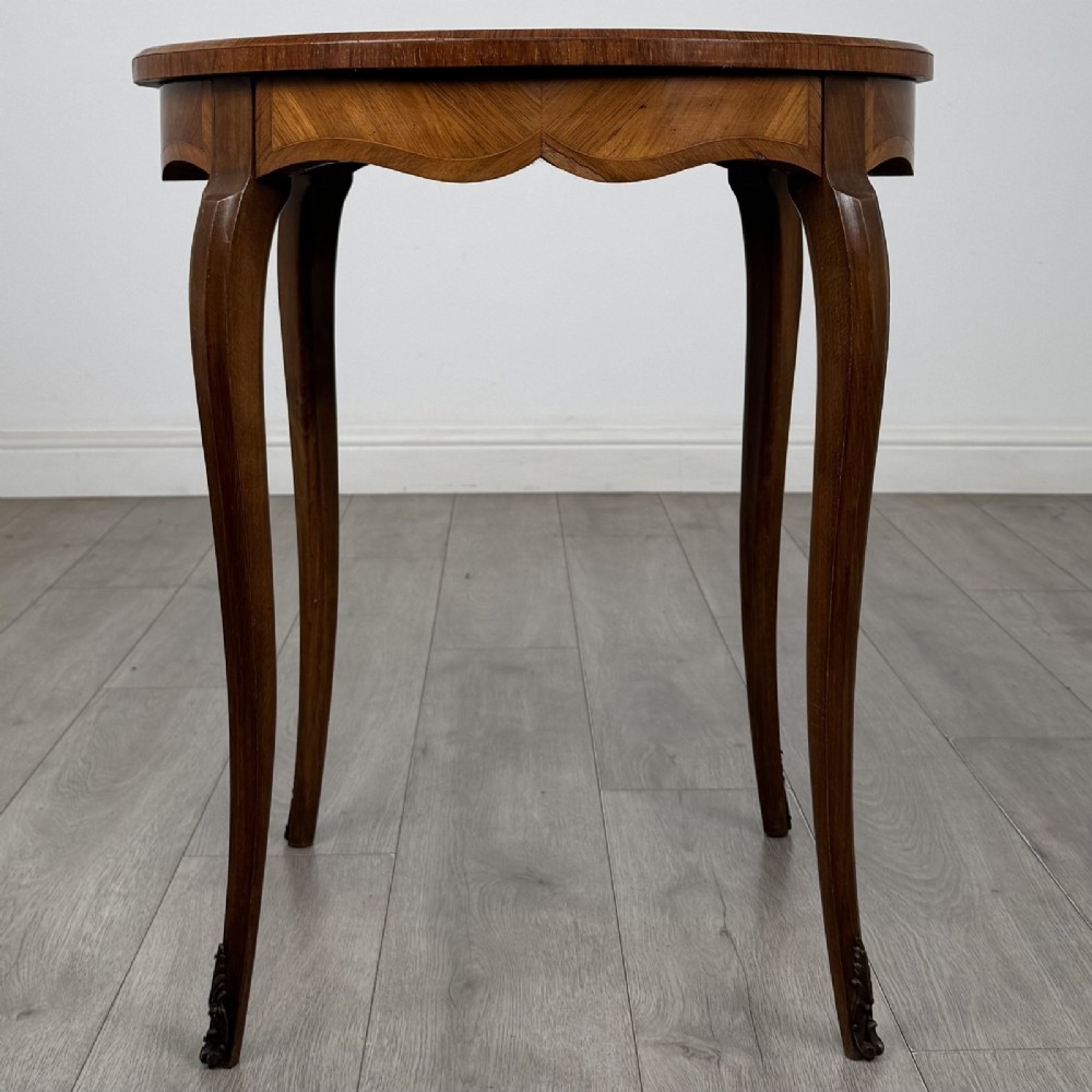 A circular French Louis XV style lamp table featuring slender cabriole legs, marquetry wood grain pattern, an undulating apron, and metal sabot feet. View V