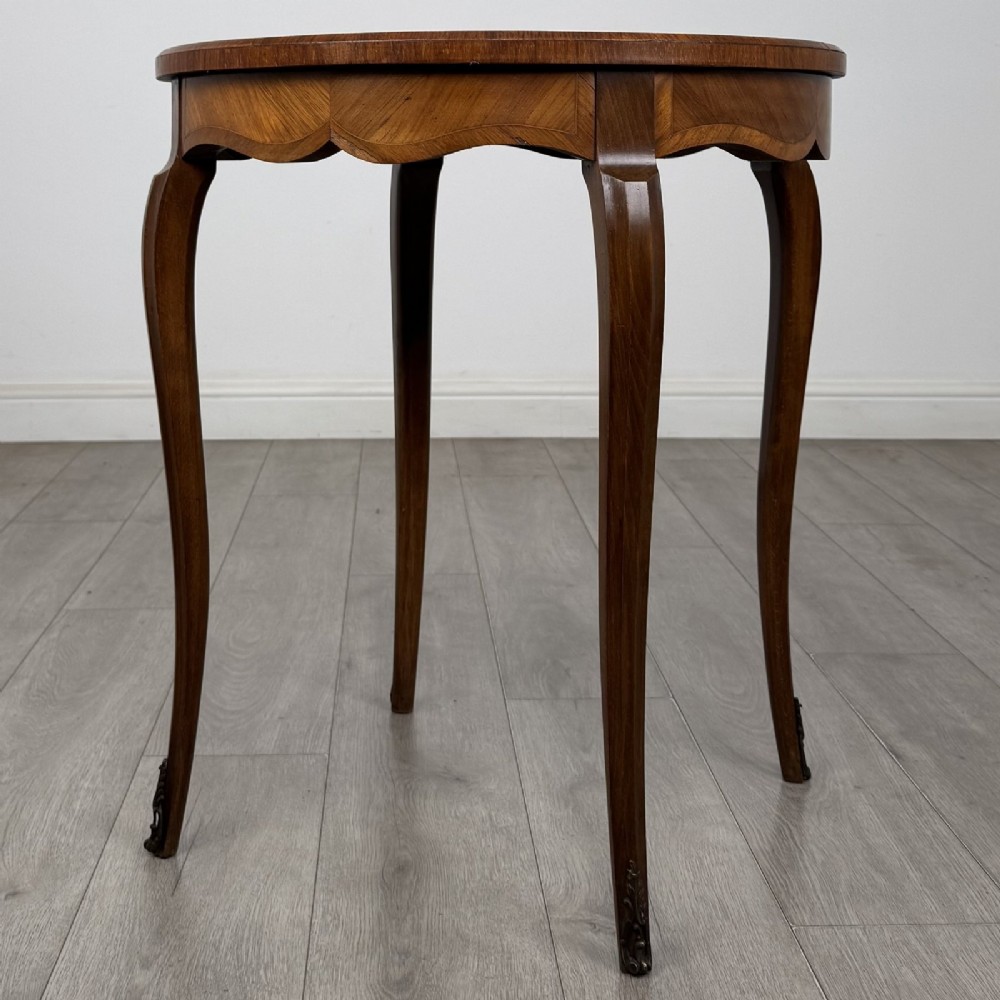 A circular French Louis XV style lamp table featuring slender cabriole legs, marquetry wood grain pattern, an undulating apron, and metal sabot feet. View VI