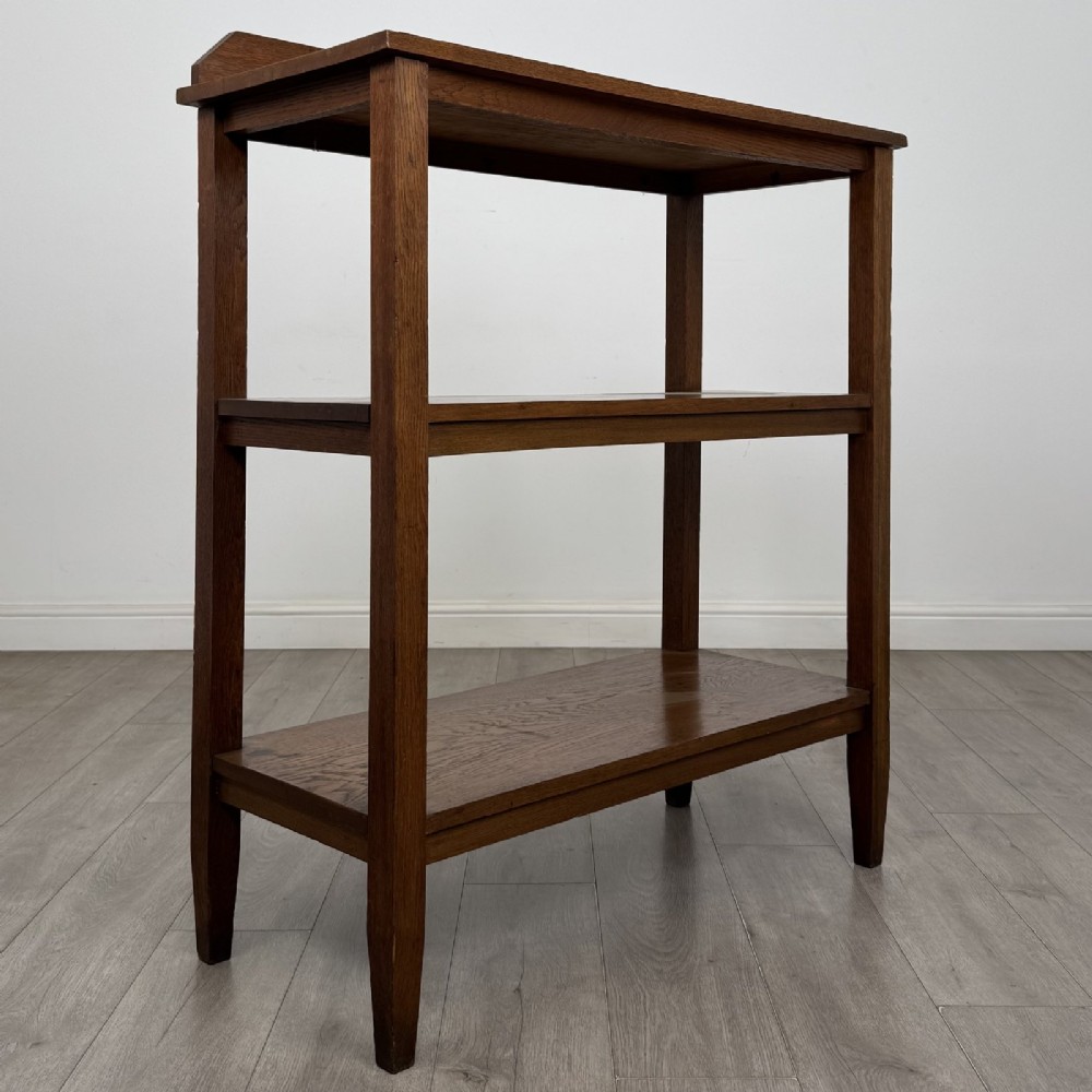 An antique Edwardian dark oak buffet featuring three open rectangular shelves supported by straight tapered legs. View VIII