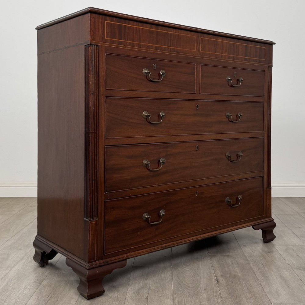 An 18th-century Georgian mahogany chest of drawers featuring inlaid stringing along the top frieze, two short drawers above three long drawers, brass swan-neck handles, fluted pilasters, and bracket feet. View VIII